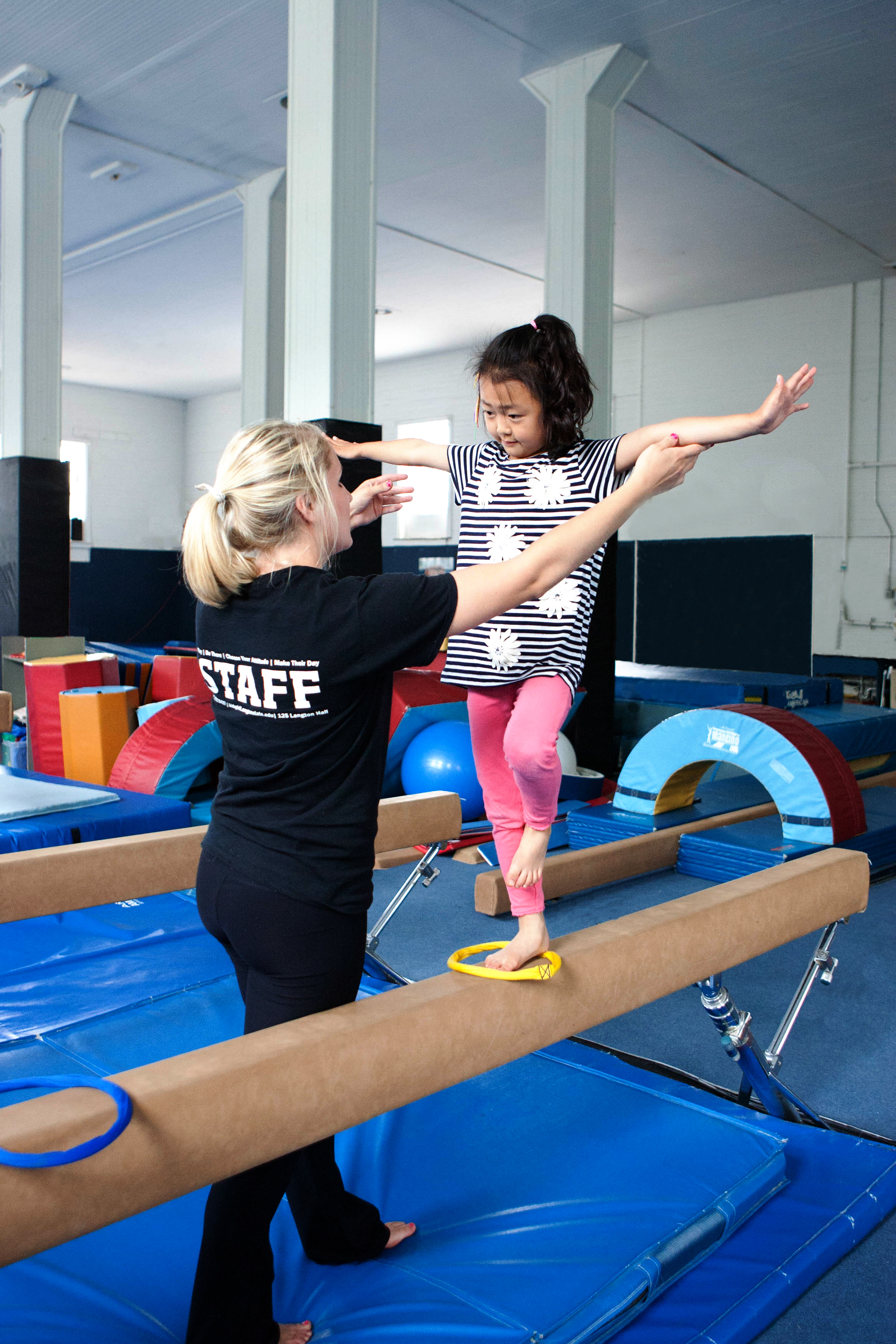 young child on balance beam with staff member coaching